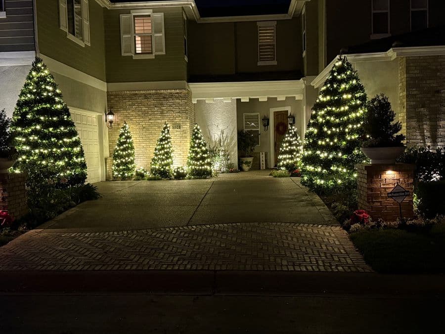 Warm white roofline lighting and lit trees at a front entry